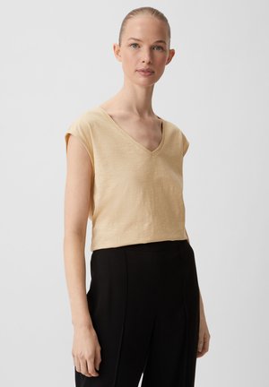 T-shirt à manches courtes, de couleur beige clair, en tissu doux, associé à un pantalon noir taille haute, présentant une coupe décontractée et une texture lisse.