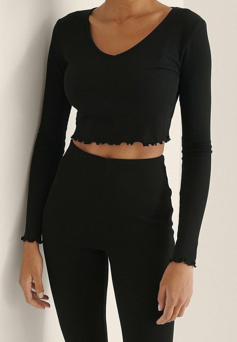 Schwarzes, geripptes, langärmeliges Crop-Top mit V-Ausschnitt und gewelltem Saum. Hergestellt aus einem dehnbaren Material, passt es eng am Körper an.