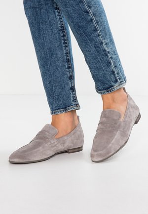 Stopy w szarych zamszowych mokasynach połączone z podwiniętymi niebieskimi dżinsami na białym tle.