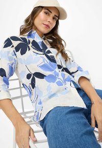 Lightweight, floral-patterned shirt in shades of blue and white, featuring a collared neckline and rolled sleeves, paired with blue jeans.