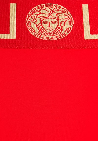 Červená látka s kruhovým zlatým emblémem s propracovanými detaily. Design obsahuje tučný text v horní části v kontrastní barvě.