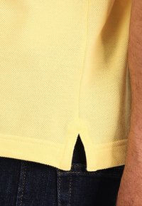 Żółta krótko-sleeve dzianinowa koszulka o fakturowanym wykończeniu i bocznymi rozcięciami u dołu, w zestawieniu z ciemnoniebieskimi dżinsami.