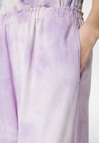 Ljuslila, batik-mönstrad tyg med en slät textur. Har ett elastiskt midjeband och sidofickor. Mjuk och flödande design.