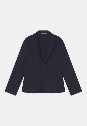 Granatowa marynarka z dwoma przednimi kieszeniami, zapięciem na jeden guzik, klapami w szpic oraz gładką teksturą materiału. Klasyczny, dopasowany krój.
