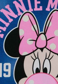 Diseño de Minnie Mouse con un gran lazo rosa con lunares, orejas negras y una cara blanca con ojos prominentes, sobre un fondo azul.