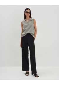 Top grigio senza maniche con colletto, abbinato a pantaloni neri larghi. Il modello indossa occhiali da sole neri e sandali neri con lacci. Design semplice e moderno.