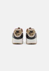 Hnedé a čierne tenisky Nike Air s textúrovaným zvrškom, vypolstrovaným golierom a bielou medzipodrážkou. Obsahuje hnedo embosované logo na podpätku.