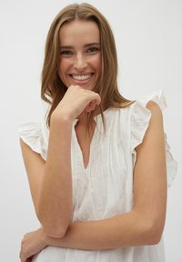 Weiße, strukturierte Bluse mit Rüschensäumen und V-Ausschnitt, die vertikale Streifen und eine lockere Passform aufweist. Glattes, leichtes Material.