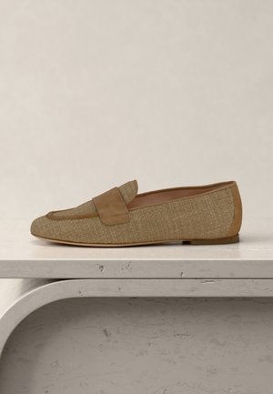 Hellbrauner gewebter Loafer mit Wildlederakzenten und flacher Sohle, platziert auf einer hellen Steinoberfläche vor neutralem Hintergrund.