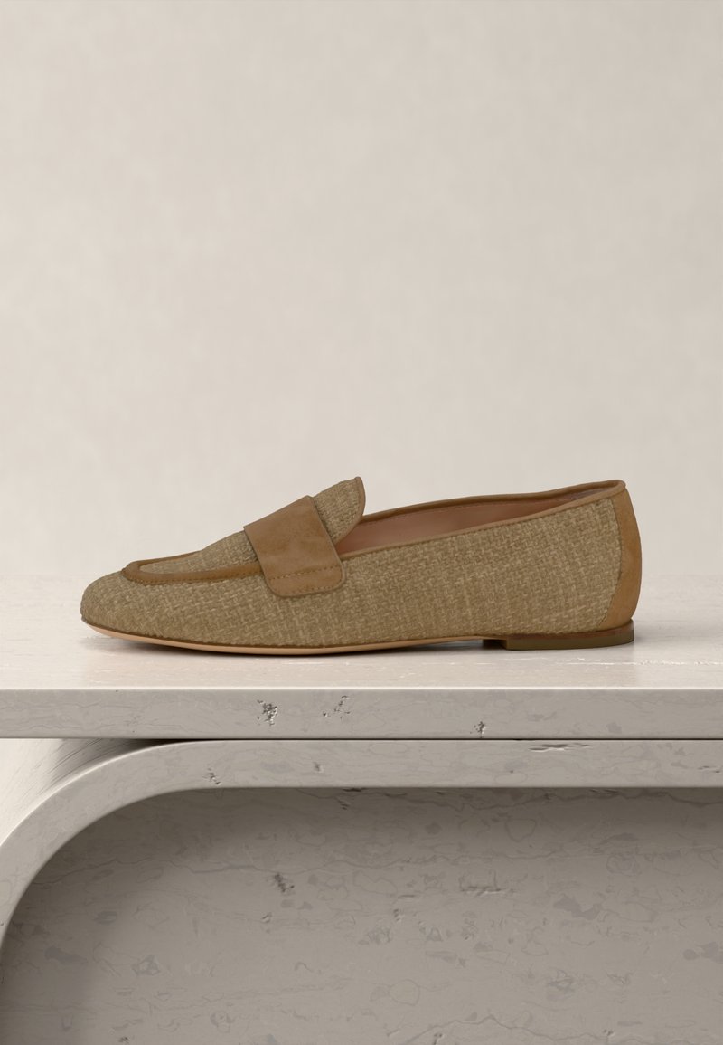 Ανοιχτό καφέ υφασμάτινο μοκασίνι με σουέντ λεπτομέρειες και επίπεδη σόλα, τοποθετημένο σε επιφάνεια από ανοιχτόχρωμη πέτρα, με ουδέτερο φόντο.