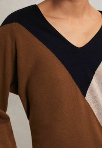 Maglione lavorato a maglia con scollo a V, caratterizzato da blocchi di colore diagonali in tonalità marrone, blu navy e beige. Tessuto morbido con una vestibilità rilassata.