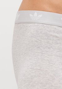 Hellgraue Sportshorts mit glatter Textur. Mit einem weißen elastischen Bund versehen, der das Adidas-Logo und ein Blattmuster aufweist.