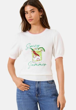 Noor naine kannab valget lühikeste varrukatega kootud toppi roosa ääristusega, rohelise ja punase litritega kokteiligraafikaga ning tekstiga „Spicy Summer“, kombineerituna siniste teksadega.
