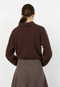 Suéter marrón suave con un cuello tipo polo, puños ajustados y una silueta relajada, combinado con una falda gris texturizada y con pliegues.