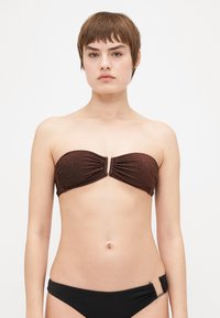 Brūns strapless bikini augšējais daļa ar rušinājuma detaļām un zeltītiem akcentiem centrā. Gluds audums ar nedaudz spīdumu pret kontrastējošu melnu apakšdaļu.