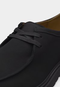 Chaussure à lacets en cuir noir avec bout arrondi et couture visible, présentée en gros plan sur un fond blanc.