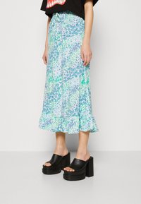 Jupe midi à motifs floraux en bleu clair et vert, avec un ourlet volanté et une taille à cordon réglable. Associée à des mules à plateforme noires.