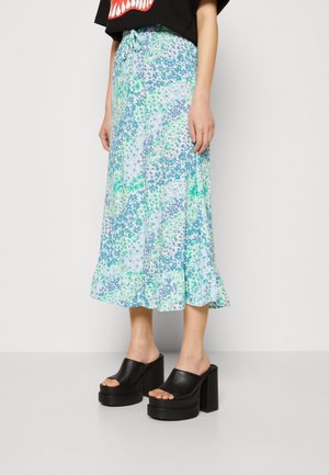 Jupe midi à motifs floraux en bleu clair et vert, avec un ourlet volanté et une taille à cordon réglable. Associée à des mules à plateforme noires.