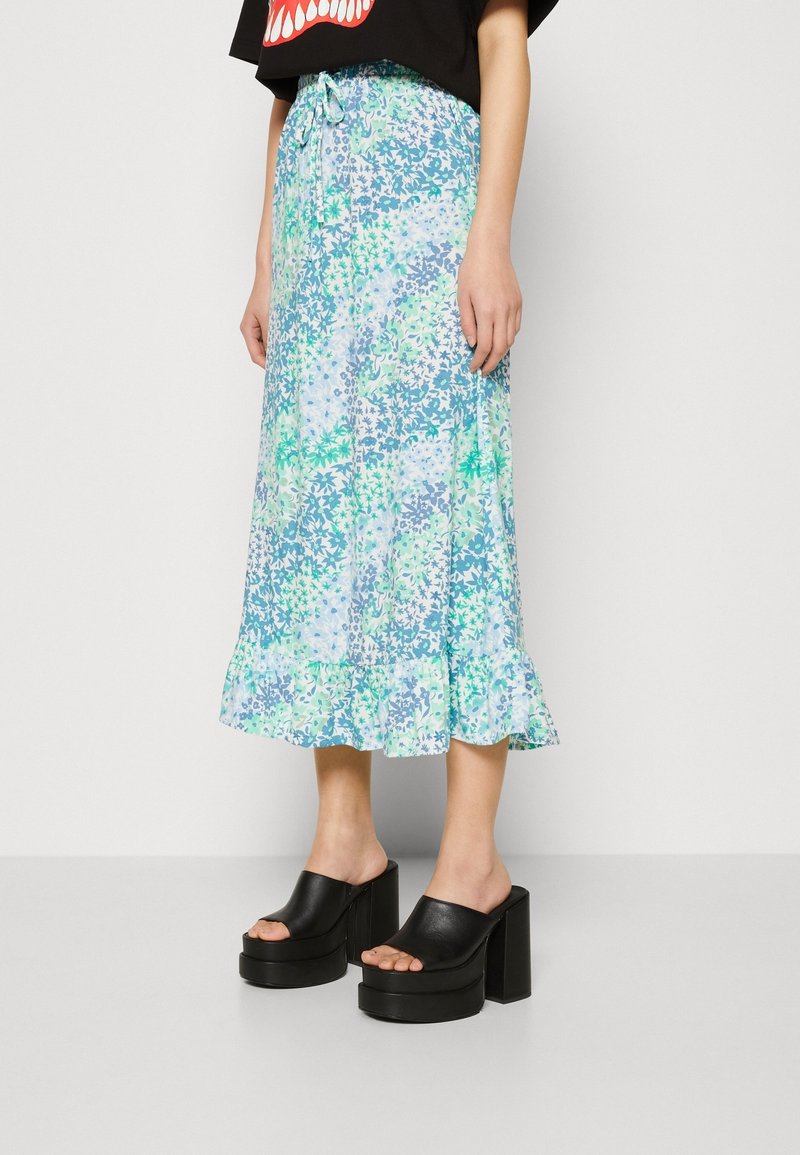 Jupe midi à motifs floraux en bleu clair et vert, avec un ourlet volanté et une taille à cordon réglable. Associée à des mules à plateforme noires.