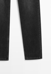 Jambes de jeans en denim noir visibles de mi-cuisse à la cheville, coupe droite avec coutures apparentes sur fond blanc.
