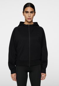 Schwarze zip-up Kapuzenjacke aus weichem Material. Verfügt über eine Kapuze, gerippte Bündchen und eine taillierte Passform. Minimalistisches Design mit eingeprägtem Logo.