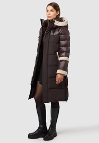 Lungo giubbotto imbottito marrone scuro con cappuccio beige foderato in pile, tasche laterali e polsini a coste. Abbinato a stivali neri al ginocchio.