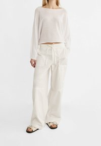 Lichtgewicht, doorschijnende witte trui met lange mouwen, gecombineerd met hoog uitgesneden, loszittende witte cargobroek met zakken en een trekkoord.