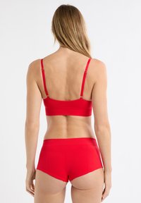 Czerwony zestaw sportowy składający się z teksturowanego biustonosza i wysokich szortów. Oba elementy mają regulowane ramiączka oraz gładki, elastyczny materiał.