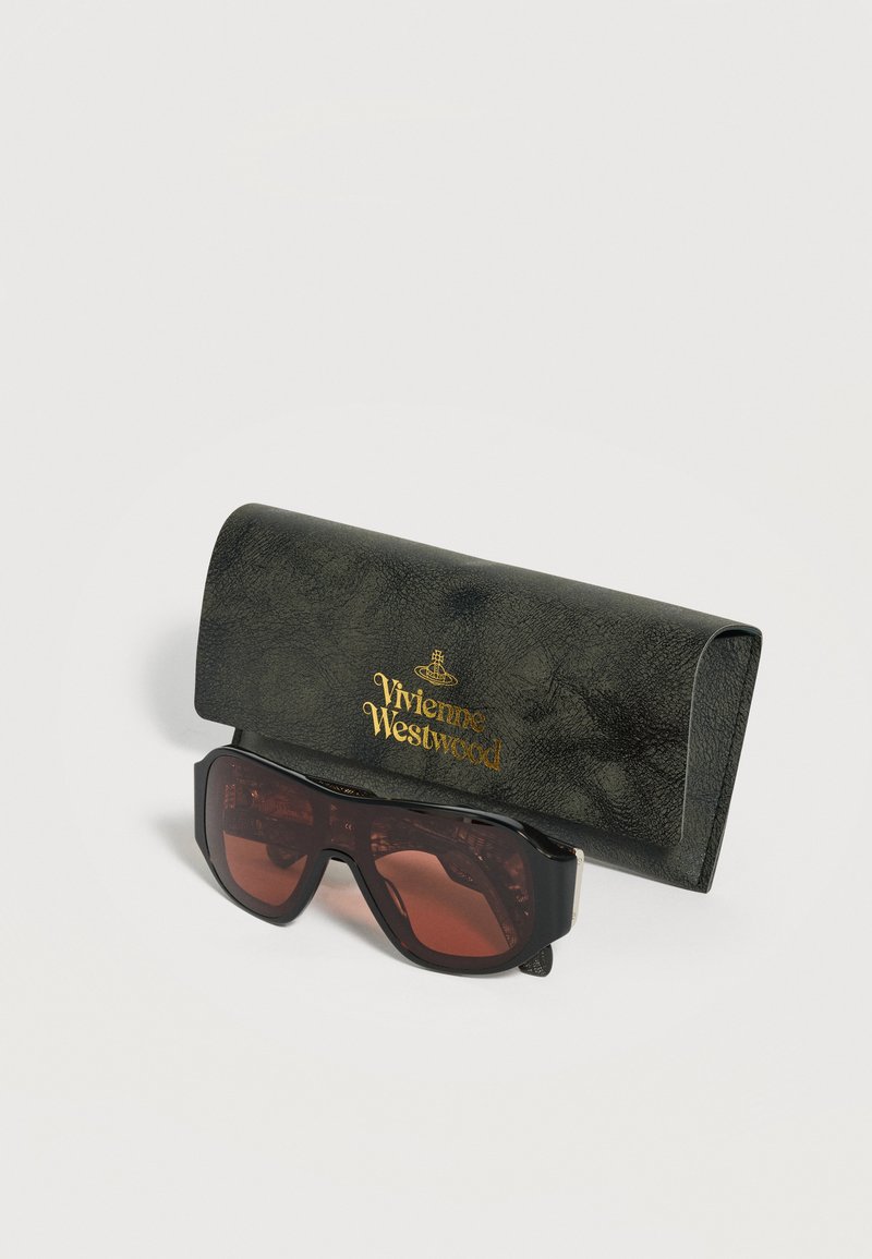 Occhiali da sole neri oversize con lenti marroni accanto a una custodia nera texturizzata Vivienne Westwood con logo dorato su sfondo bianco.