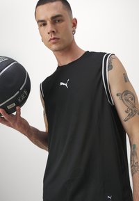 Μαύρο αμάνικο αθλητικό μπλουζάκι με λευκές ρίγες, που φέρει το λογότυπο Puma στο στήθος. Το μοντέλο κρατάει μια μπάλα μπάσκετ.