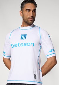 Camiseta deportiva blanca con detalles en azul, que presenta un logo "RACING" y texto "betsson". Mangas cortas y escote redondo, hecha de tela lisa.
