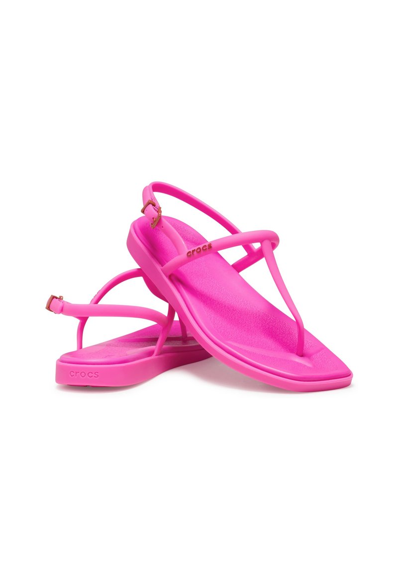 Różowe sandały Crocs o eleganckim designie, płaskiej podeszwie, pasku między palcami oraz skrzyżowanych paskach; wykonane z lekkiego, teksturowanego materiału.
