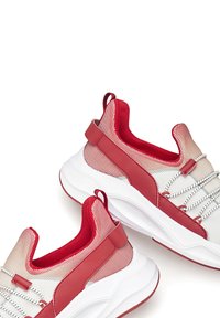 Red and white sneakers featuring a mesh upper, padded collar, and textured rubber sole with looped heel pull tab and elastic laces.