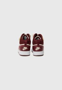 Nike tenisice u burgundcu i krem boji, s teksturiranim gornjim dijelom, podstavljenim ovratnikom i bijelim potplatom s vidljivim logom na peti.
