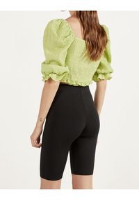 Zelený texturovaný crop top s nabíranými rukávy a řaseným lemem, ve spojení s černými cyklistickými šortkami s vysokým pasem.