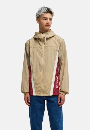 Beige lightweight jacket with a hood, featuring maroon and white diagonal stripes and logo on the lower right side. Textured fabric.