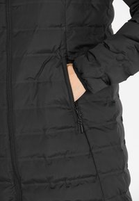 Sort polstret jakke med en quiltet design, der har lynlås og sidelommer. Materialet er glat med en mat overflade.