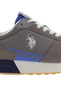 Grå mockaskor med blå detaljer, gummisula, vita snörningar och en polo-spelare logga på sidan. Texturerad ovandel med lagerdesignselement.