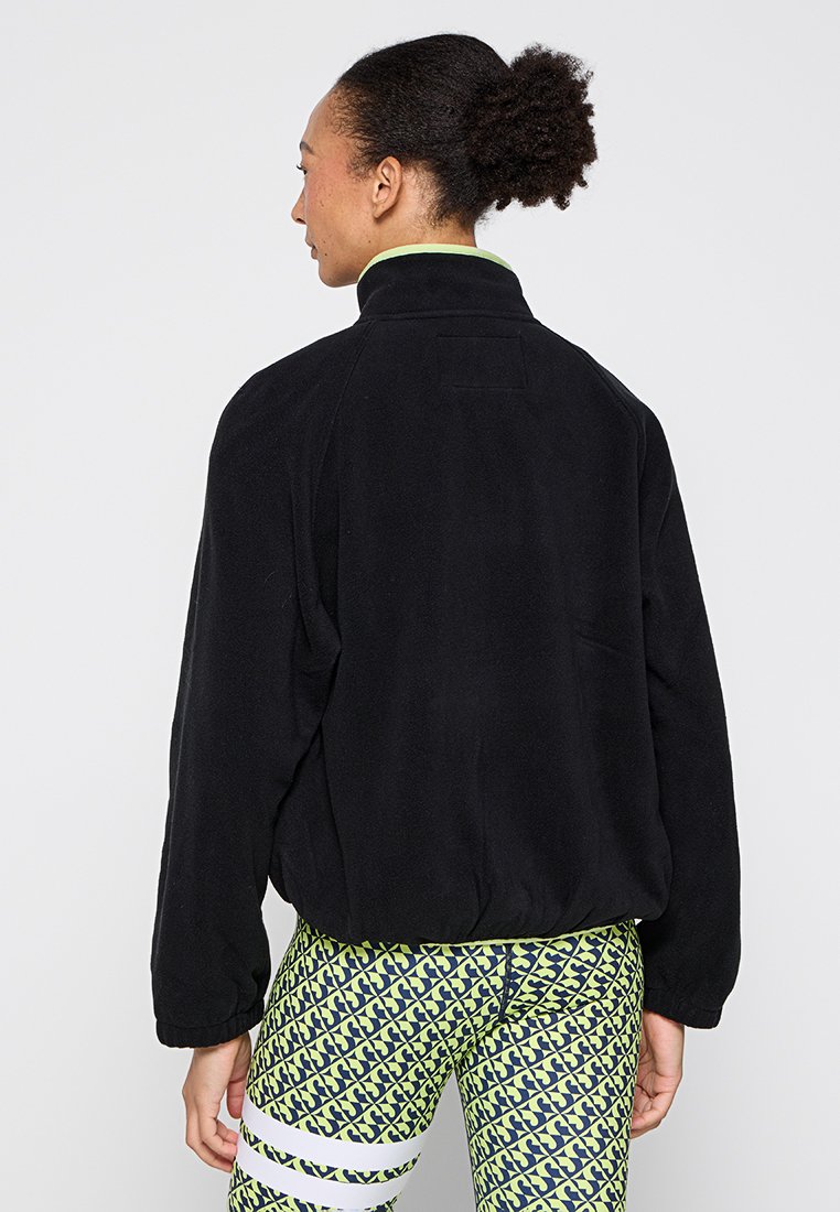 Schwarze Fleecejacke mit hohem Kragen und legerer Passform. Sie hat eine glatte Textur und ein kleines Stoffetikett auf der Rückseite.