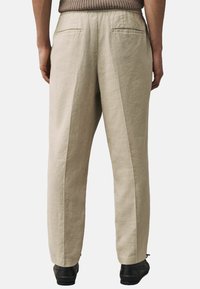 Pantalons en lin beige avec une coupe décontractée, dotés de deux poches arrière et d'une texture lisse. Des plis centraux s'étendent le long des deux jambes.