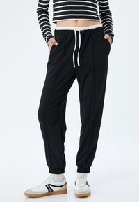 Zwarte joggers met een witte trekkoord en elastische manchetten, met een soepele textuur en een taps toelopend ontwerp.
