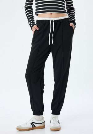 Zwarte joggers met een witte trekkoord en elastische manchetten, met een soepele textuur en een taps toelopend ontwerp.