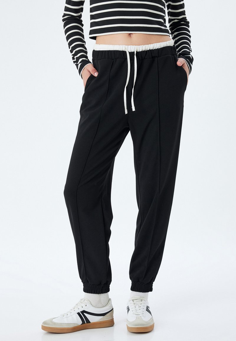 Zwarte joggers met een witte trekkoord en elastische manchetten, met een soepele textuur en een taps toelopend ontwerp.