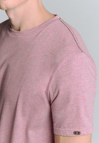 Roze gemêleerde t-shirt met korte mouwen en een ronde halslijn, voorzien van een klein logolabel op de linkermouw en subtiele stikdetails.