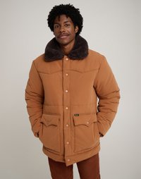 Bruine pufferjack met een donkere bontkraag, drukknopen en twee klepzakken. Zachte textuur en een ontspannen pasvorm.