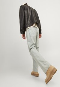 Svart skinnjakke, beige genser, lyseblå jeans med avslappet passform, og brune kraftige støvler, sett bakfra.