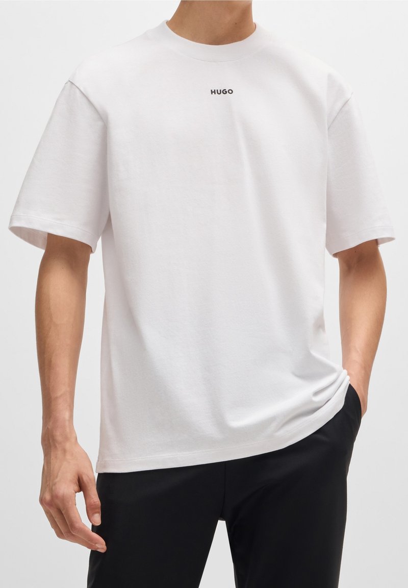 Biała bawełniana koszulka z okrągłym dekoltem i krótkimi rękawami, z małym czarnym logo "HUGO" umieszczonym na środku klatki piersiowej.