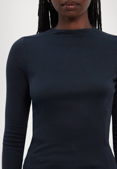 Marineblå langærmet bluse lavet af ribbet stof, med høj halsudskæring og tætsiddende silhuet med minimal sømdetaljering.