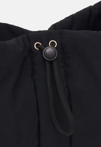 Cordon en tissu noir avec un bloqueur en plastique et des œillets dorés, présentant une surface texturée et des détails de couture visibles.