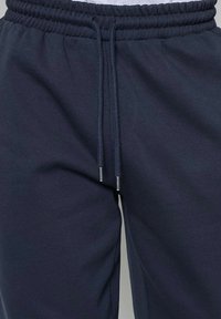 Pantalons de survêtement bleu marine en mélange de coton doux, présentant une taille élastique avec cordon de serrage et embouts en métal argenté. Texture lisse.